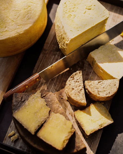 Assorted cheeses, including wheels and wedges, displayed on a wooden board, accompanied by a knife, showcasing a variety of textures and colors.