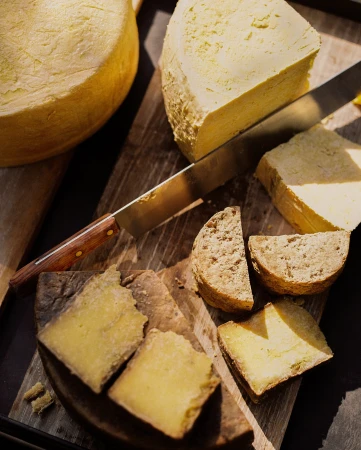 Assorted cheeses, including wheels and wedges, displayed on a wooden board, accompanied by a knife, showcasing a variety of textures and colors.