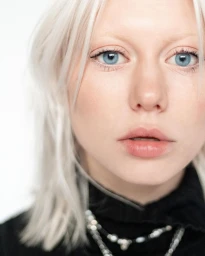 Close-up portrait of a woman with white hair, blue eyes, and black top against white background