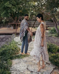 A smiling woman in a light patterned dress and a man in a patterned poncho walking along a stone garden path, photographed by Bethany Reed