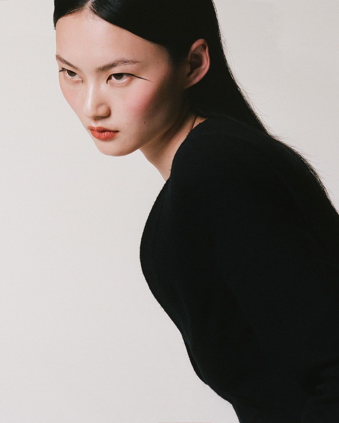 Portrait of an Asian female model in a black top against a white backdrop in a photo studio with editorial styling, showcasing her visage.