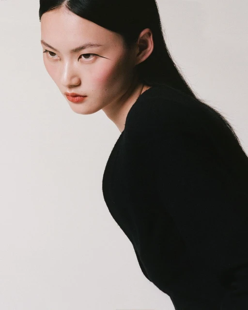 Portrait of an Asian female model in a black top against a white backdrop in a photo studio with editorial styling, showcasing her visage.