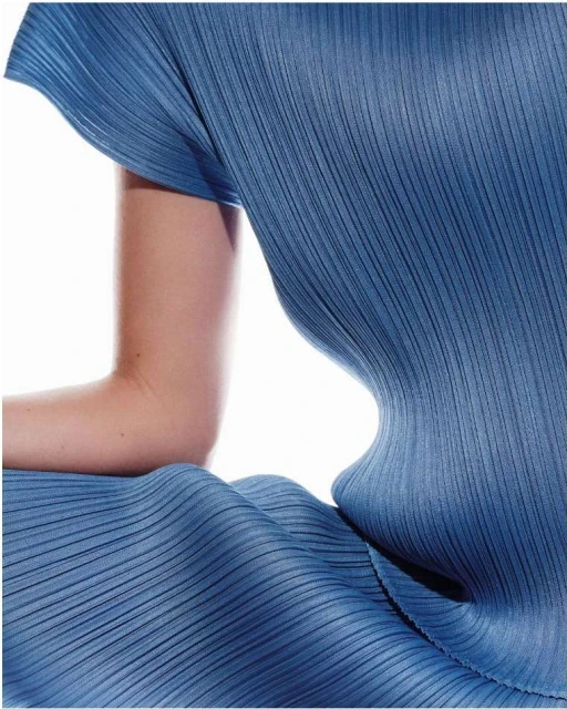 Closeup of a female torso wearing a textured blue dress. The fabric has vertical pleats and creates an abstract design with light and shadow.