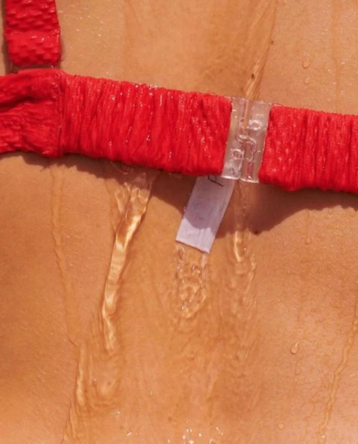 Close-up view of a torso wearing a red top with water running down the skin, highlighting texture and form in a bright, natural light.