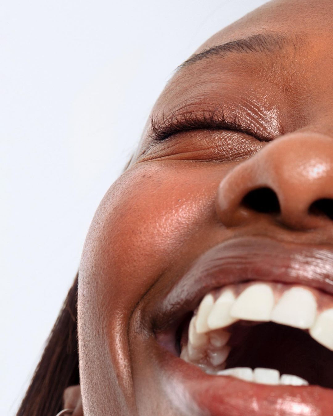 Close-up portrait of a smiling adult woman with dark skin and an open mouth, revealing her teeth, against a clean white background.