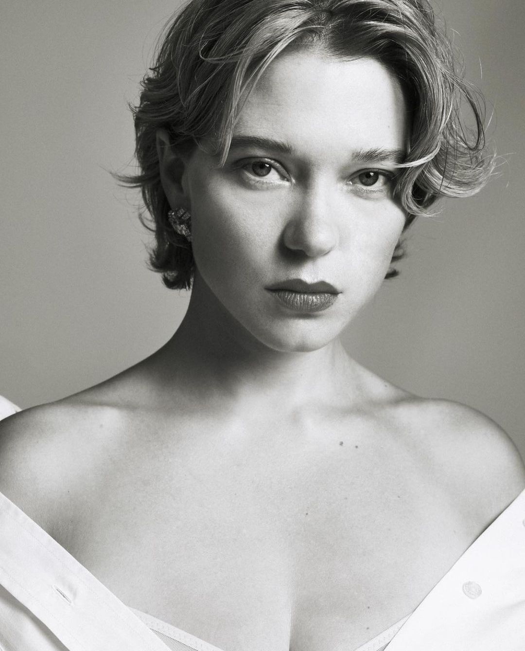 Portrait of actress Lea Seydoux with short blonde hair and earrings wearing an off-the-shoulder white top
