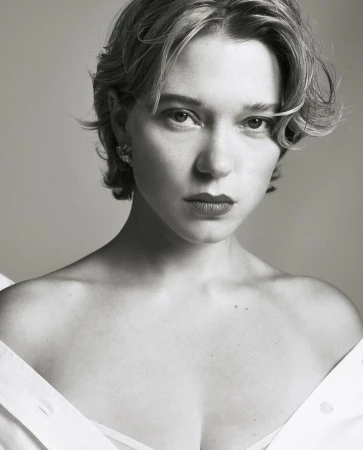 Portrait of actress Lea Seydoux with short blonde hair and earrings wearing an off-the-shoulder white top