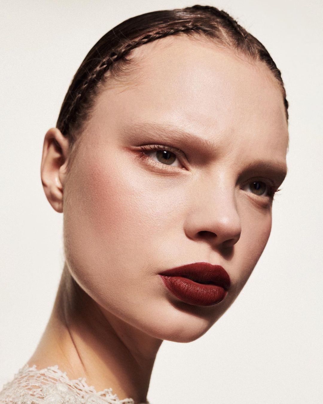 Close-up portrait of a woman with dark braided hair and deep red lipstick against a plain white background by Betina Du Toit