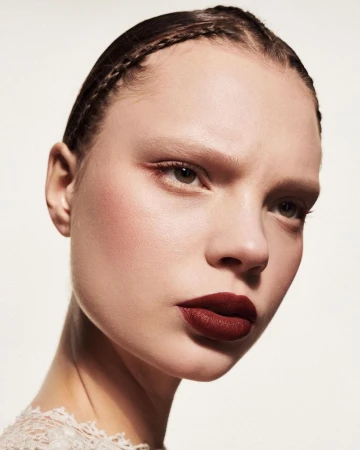 Close-up portrait of a woman with dark braided hair and deep red lipstick against a plain white background by Betina Du Toit