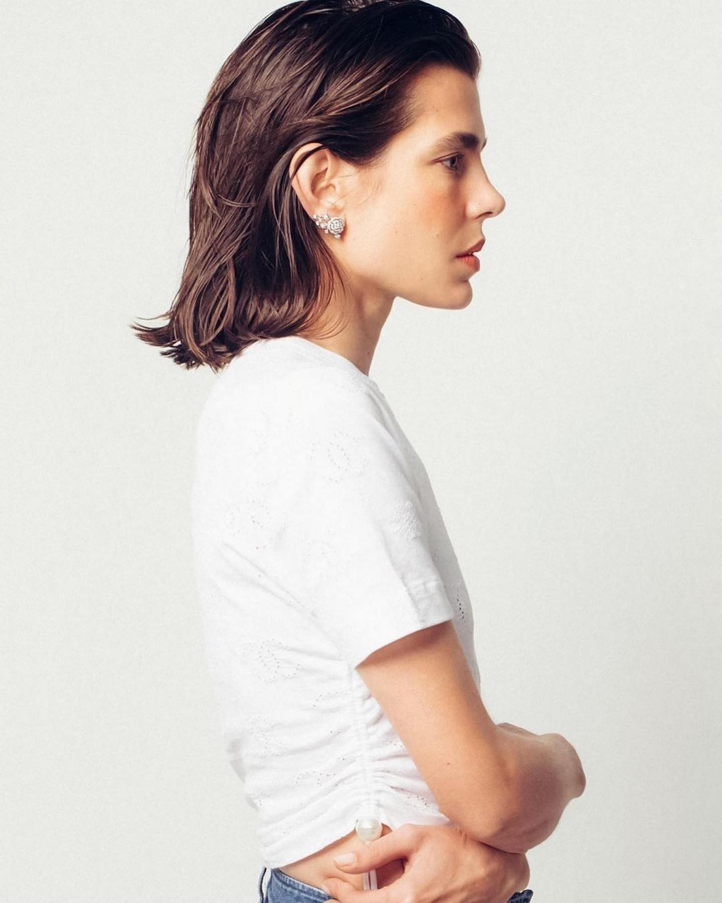 Profile shot of an adult woman with dark hair wearing a white top with subtle floral details against a plain white backdrop.