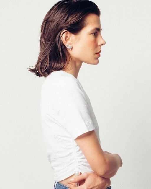 Profile shot of an adult woman with dark hair wearing a white top with subtle floral details against a plain white backdrop.