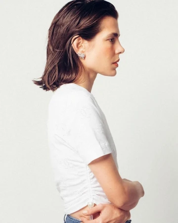 Profile shot of an adult woman with dark hair wearing a white top with subtle floral details against a plain white backdrop.