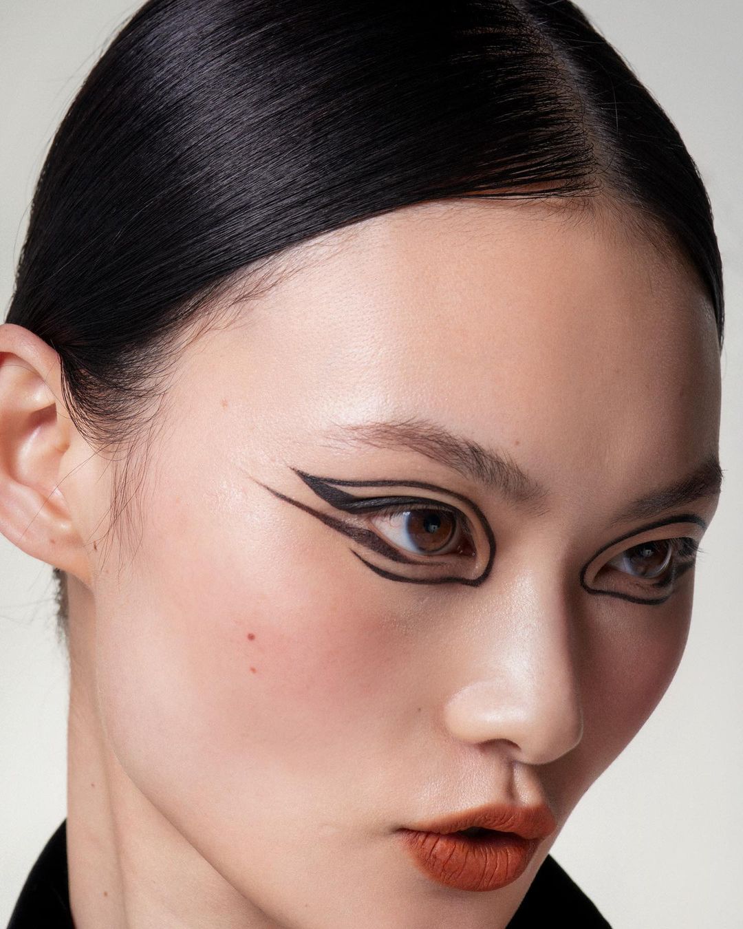 Close-up beauty shot of an adult woman with dramatic black graphic eye makeup against a neutral background. Beauty and makeup concept.