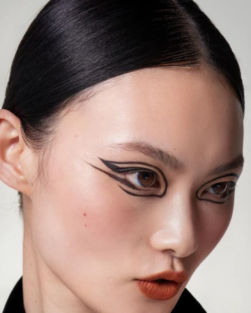 Close-up beauty shot of an adult woman with dramatic black graphic eye makeup against a neutral background. Beauty and makeup concept.