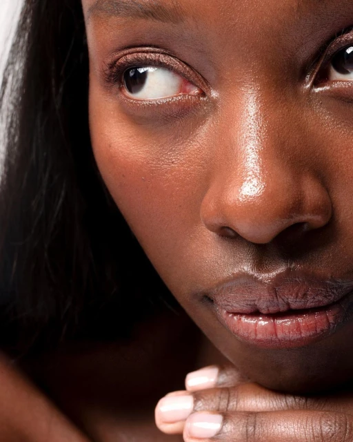 Close-up portrait of an adult woman with dark skin, showcasing her face, natural makeup, and sleek black hair against a white backdrop.