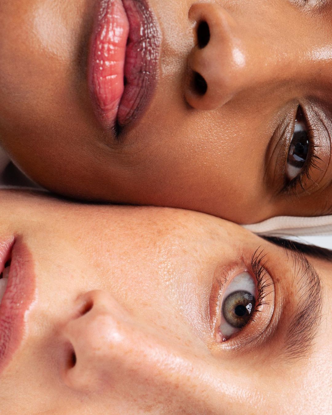 Close-up studio shot features two adult women with diverse skin tones, highlighting makeup, beauty, and skincare. Eye-level perspective.