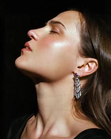 Close-up profile of a woman with her eyes closed, wearing an ornate art deco drop earring, captured against a black background.