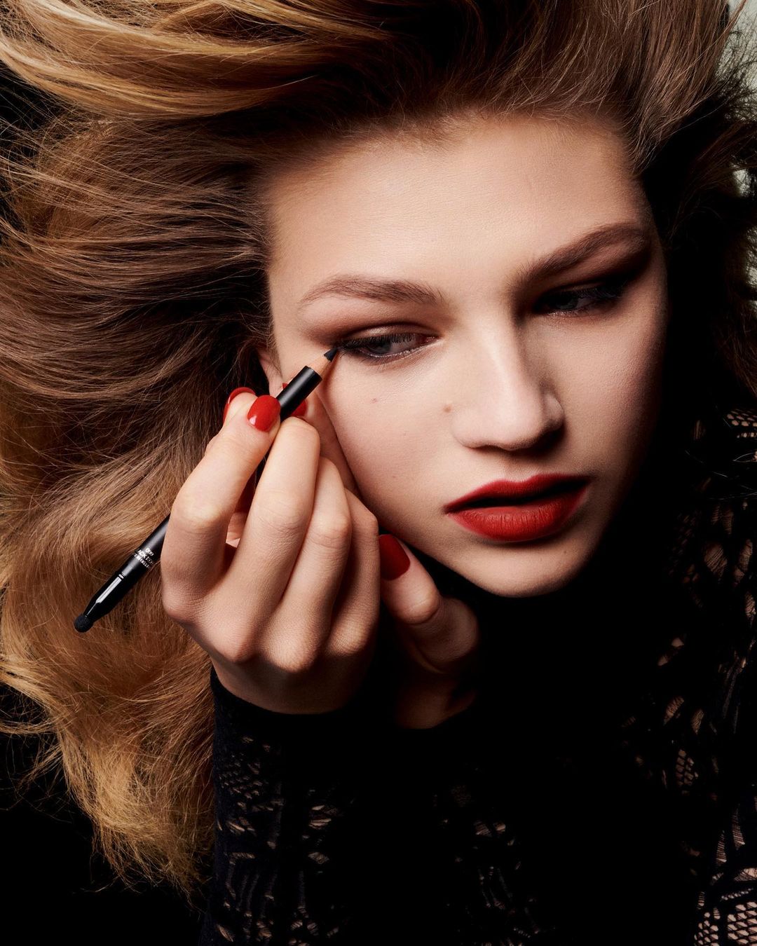 Close-up shot of a woman applying eyeliner with red nails and lips; beauty and make-up industry concept for beauty, fashion, and lifestyle.