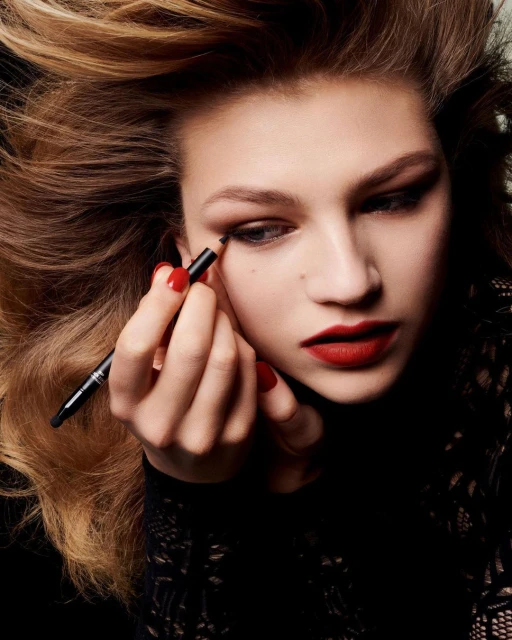 Close-up shot of a woman applying eyeliner with red nails and lips; beauty and make-up industry concept for beauty, fashion, and lifestyle.