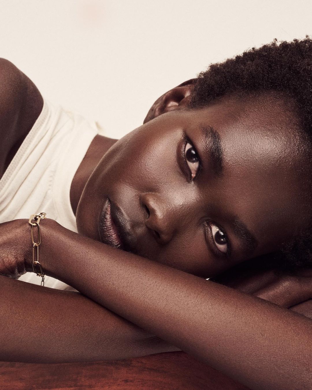 Close-up studio shot of an African-descent adult female model with short natural hair, lying down with a gold bracelet on her wrist.