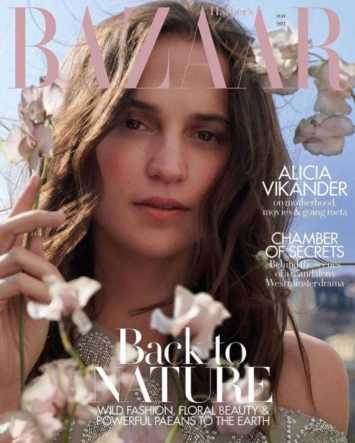 Alicia Vikander on the cover of Harper's Bazaar May 2022 issue. She is surrounded by white flowers, and the magazine title is visible.