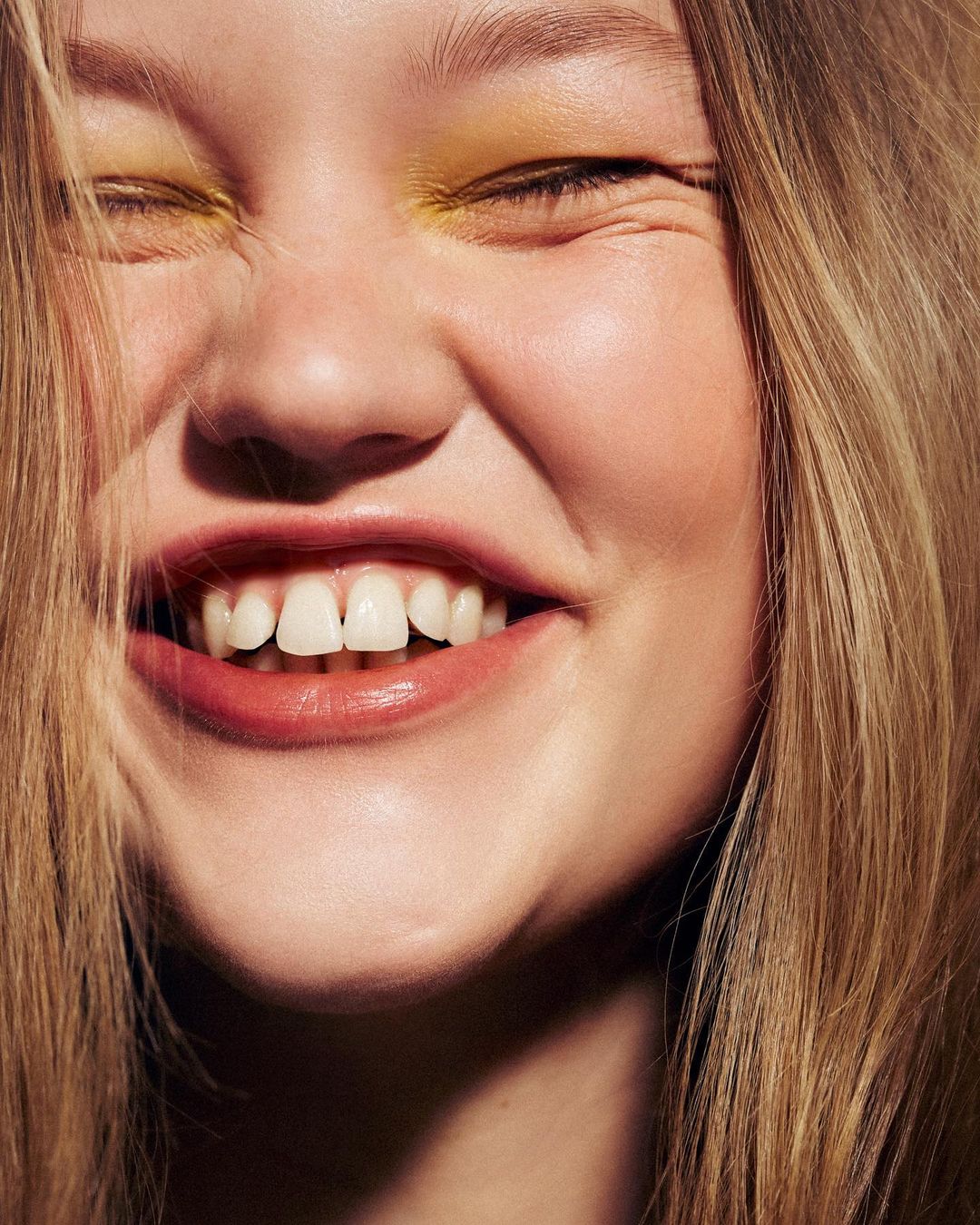 Close up portrait of a smiling woman with blonde hair and yellow eye shadow photographed by Betina Du Toit