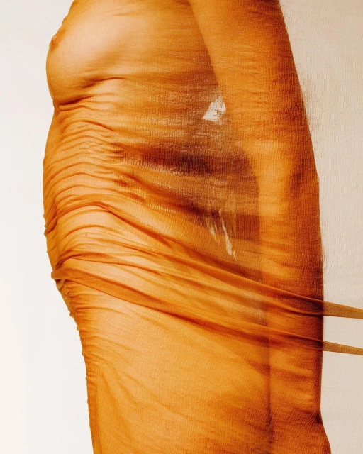 A nude adult female is tightly wrapped in an orange, semi-transparent fabric, in a close-up studio shot against a plain white background.