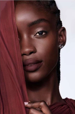 Close-up portrait of a Black woman holding a sheer burgundy fabric across the left side of her face, by Betina Du Toit.