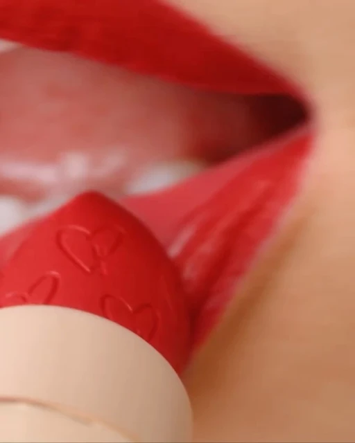 Macro shot of red lipstick application on lips with heart pattern detail on the lipstick bullet, close-up of the mouth.