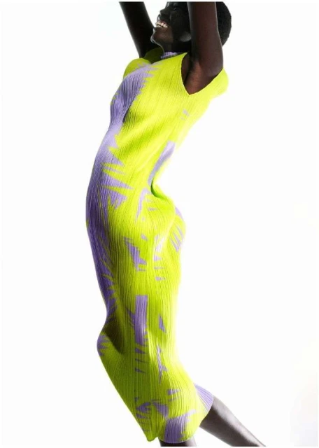 An adult woman in a sleeveless patterned midi dress smiles and raises her arms against a bright white background in a fashion portrait.