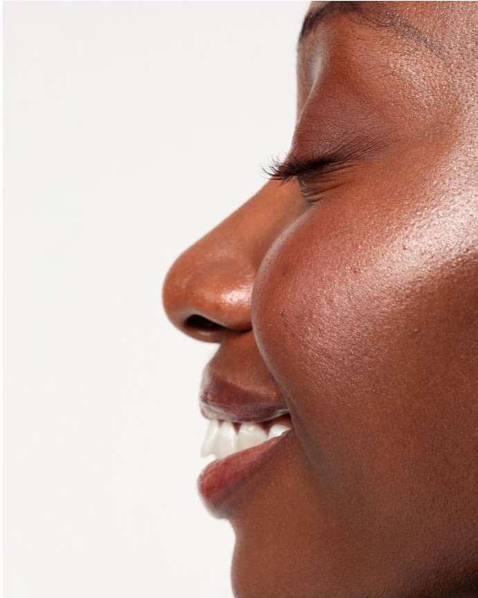 Close-up portrait of an African American woman with brown skin, white teeth, and a natural beauty look against a clean white background.