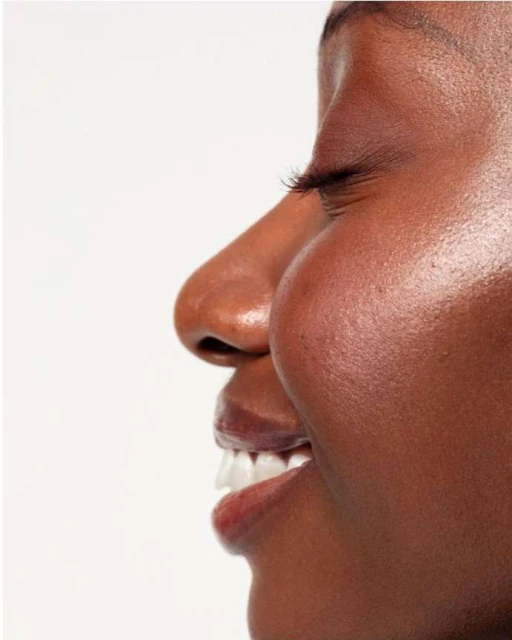 Close-up portrait of an African American woman with brown skin, white teeth, and a natural beauty look against a clean white background.