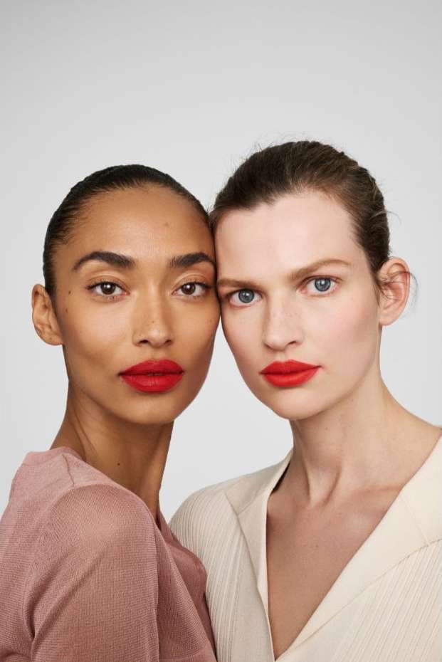 Close-up of two women with red lipstick posing in a studio setting. One model has dark skin and the other has light skin.