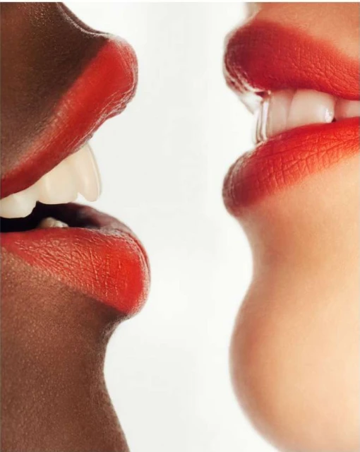 Close-up of two women of different ethnicities with red lipstick, teeth showing, against a white background, conveying a sense of diversity.