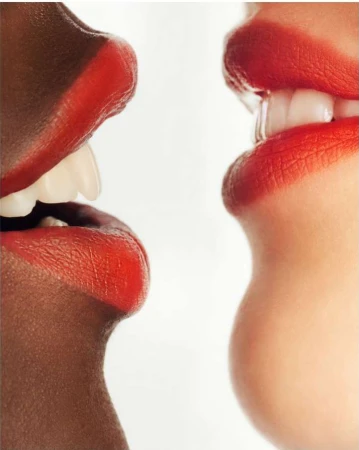 Close-up of two women of different ethnicities with red lipstick, teeth showing, against a white background, conveying a sense of diversity.