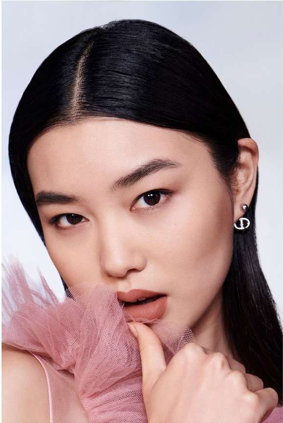 Close-up of an Asian woman with dark hair and neutral makeup, wearing a pink tulle top and earrings. Beauty, cosmetics, fashion.