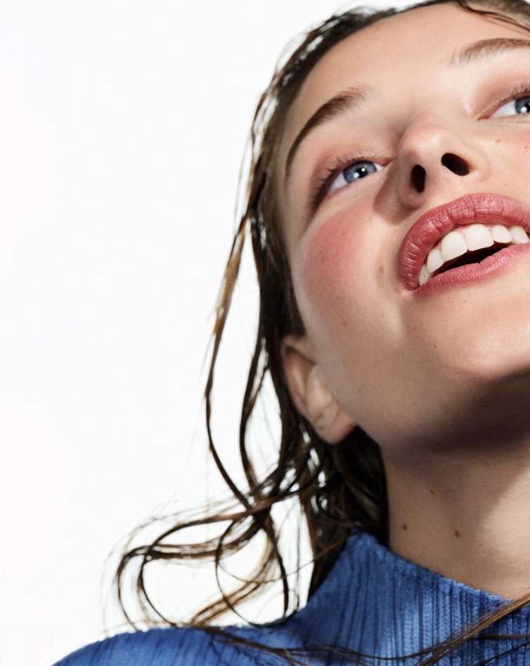 Close-up portrait of a woman with wet hair wearing a blue textured top against a white background by Betina Du Toit