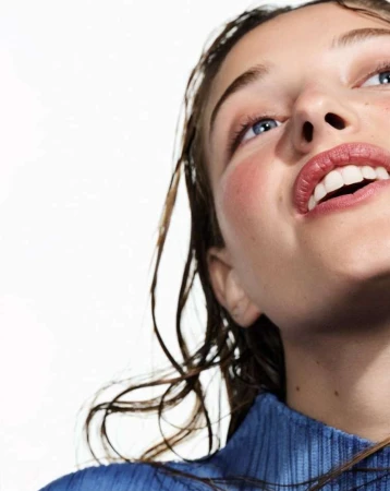 Close-up portrait of a woman with wet hair wearing a blue textured top against a white background by Betina Du Toit
