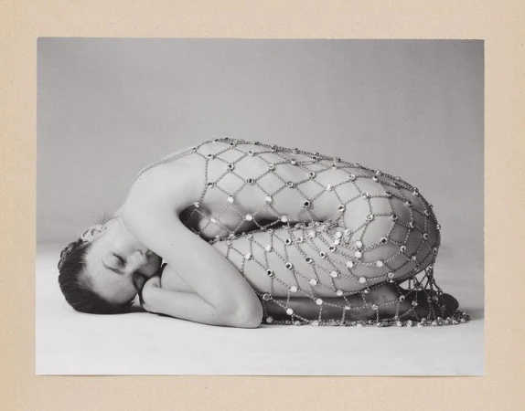 Monochrome portrait of a reclined woman covered in a mesh chain with jewels against a neutral background in a studio setting.