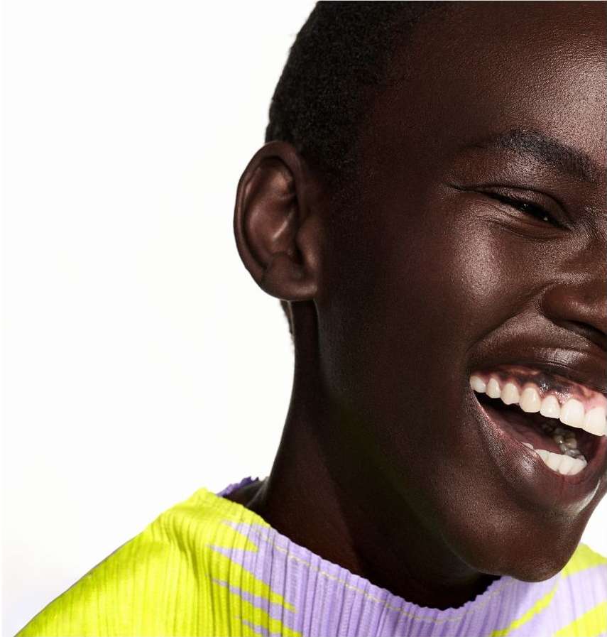 Close-up portrait of a smiling African American adult female wearing a bright neon yellow and light purple shirt against a white background.