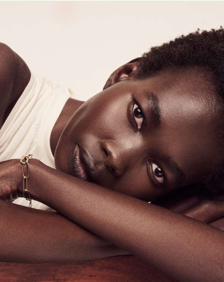 Close-up portrait of a black female adult with short curly hair wearing a bracelet, lying down with her face toward the camera in a studio.