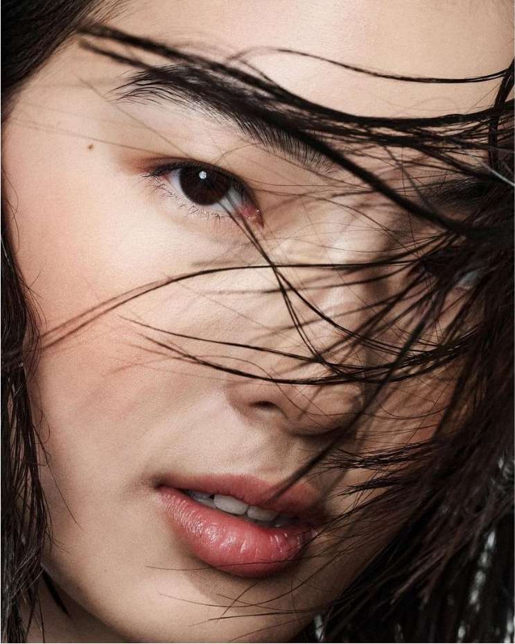 Close-up beauty portrait of a woman with wet dark hair strands falling across her face shot by Betina Du Toit