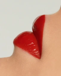Extreme close-up macro view of glossy red lipstick on lips against a neutral background by Betina Du Toit