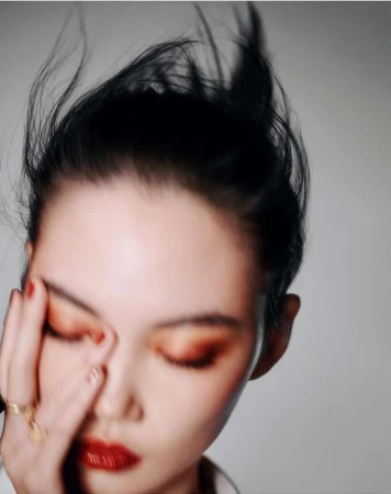Close-up beauty portrait of a woman with red lipstick and dark hair catching the wind against a grey background.