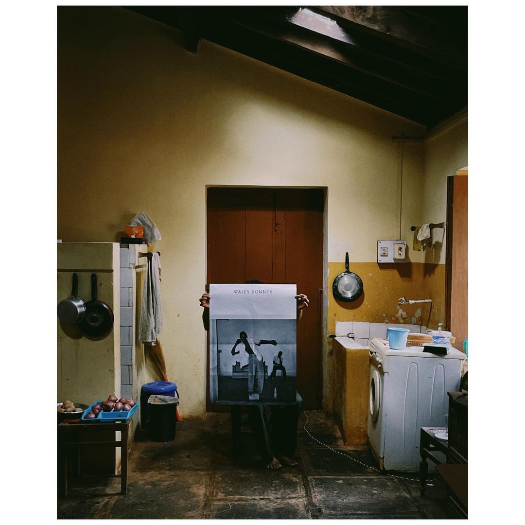 Indoor shot of a person holding up a poster featuring black and white photos in a residential space with a kitchen and dark wooden roof.