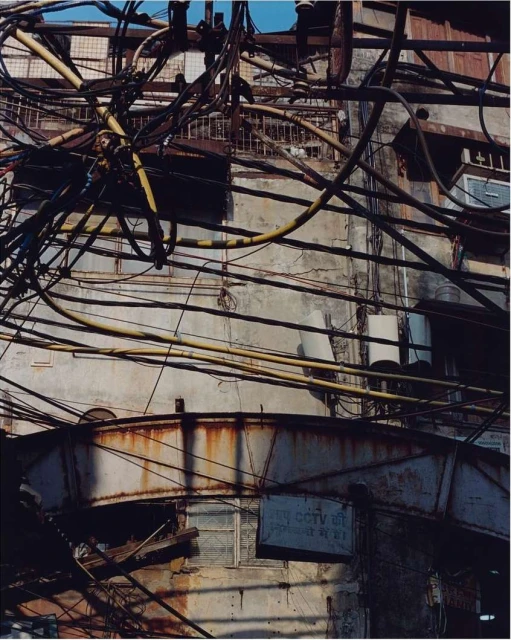 Exterior of an old building with peeling paint and rust, crisscrossed by a dense network of electrical wires and signage in daylight.