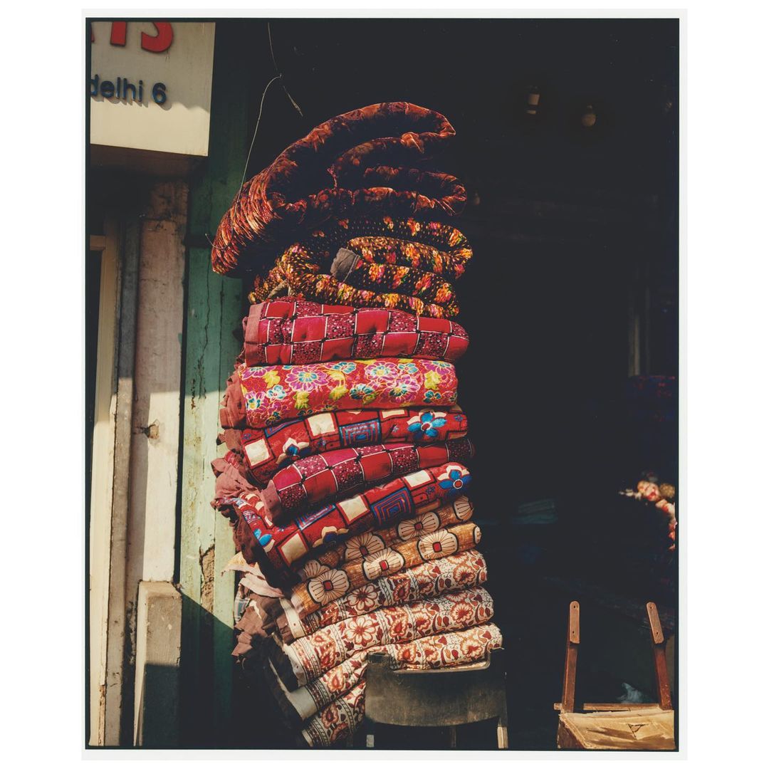 A stack of neatly folded, colorful, patterned blankets hanging in front of a dark doorway, casting soft shadows on the adjacent white wall.