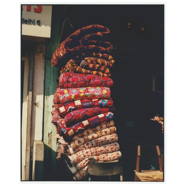 A stack of neatly folded, colorful, patterned blankets hanging in front of a dark doorway, casting soft shadows on the adjacent white wall.
