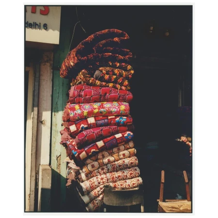 A stack of neatly folded, colorful, patterned blankets hanging in front of a dark doorway, casting soft shadows on the adjacent white wall.