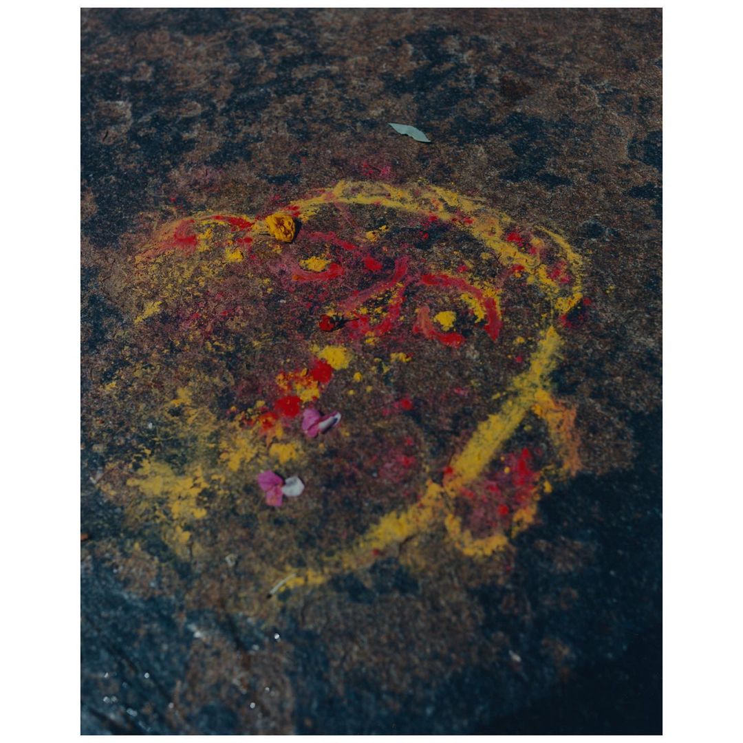 Red and yellow powder design on a dark stone surface featuring a circular outline and floral accents, photographed with a high angle.